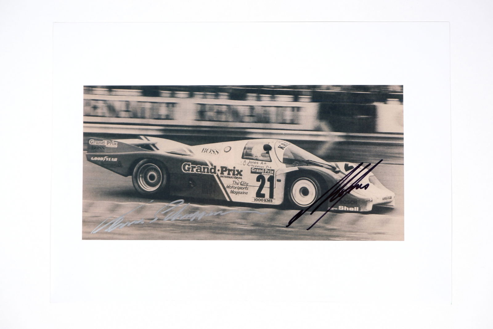 JONES/SCHUPPAN: Image of Jones & Schuppan racing a Kremer Porsche 956. Jones & Schuppan signatures: JONES/SCHUPPAN: A black and white image of Alan Jones and Vern Schuppan racing a Kremer Porsche 956 at Le Mans, image signed by Jones in black, Schuppan signature in silver; on photographic paper, ima