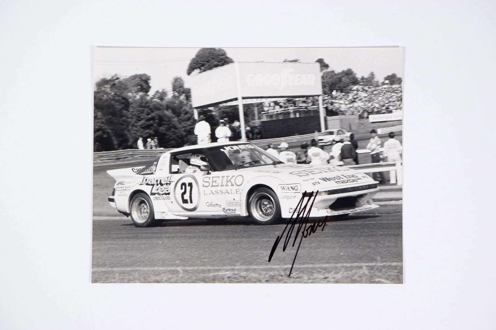 JONES: Photograph by AUTOPIX, depicting Alan Jones in a SA22C Group C Mazda RX7. A.J signature: JONES: An original black and white photograph by AUTOPIX - Ian Smith & Associates - depicting Alan Jones in a SA22C Group C Mazda RX7, image signed by Jones; image measures approximately 21.5cm wide,