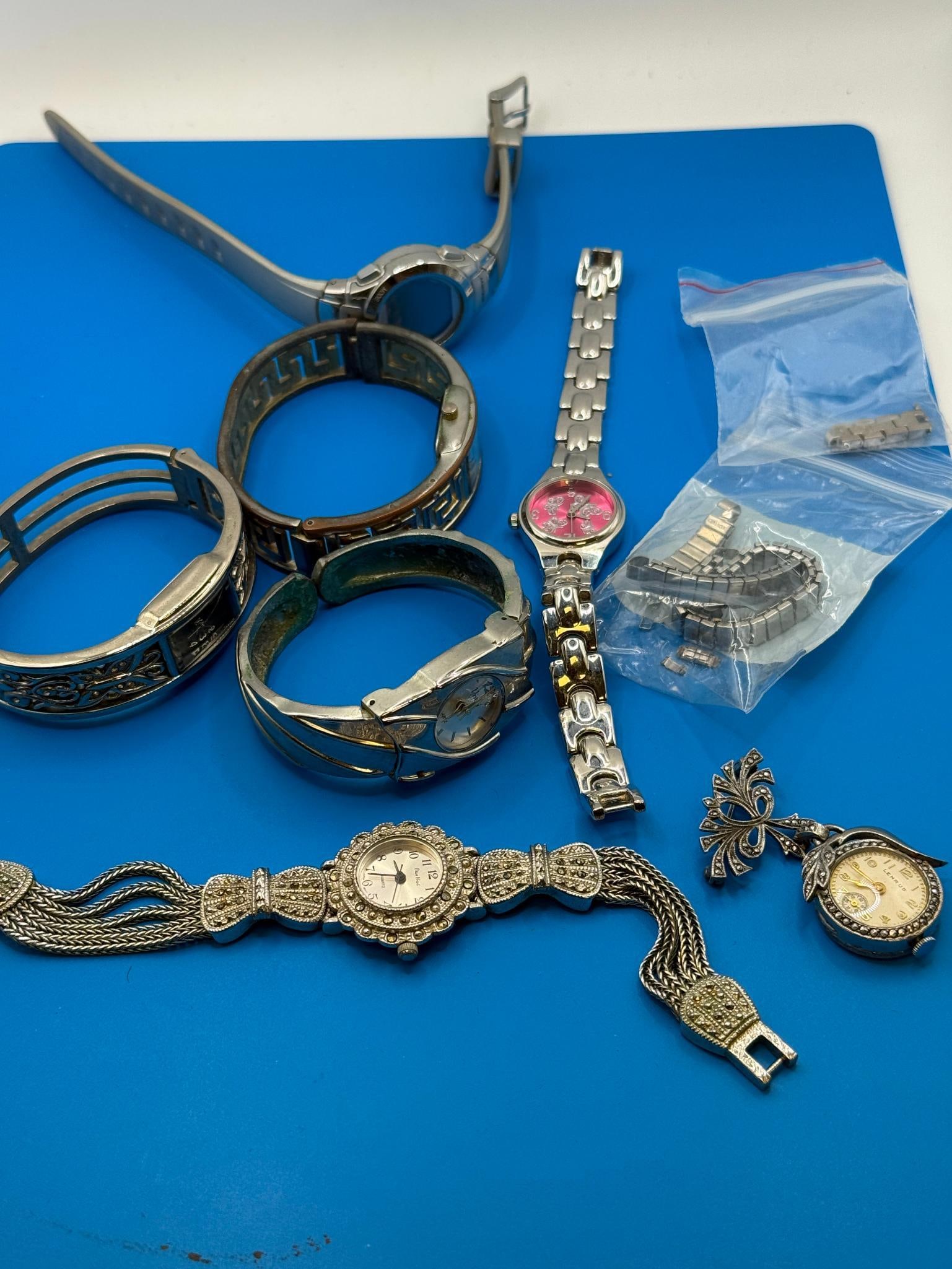 Collection of Women's Watches w/ Metal Bands, Multiple Brands Incl.Timex, brooch pin marked Sterling: This collection features a variety of women's watches with metal bands, including brands like Timex. The set includes various dial colors such as black, pink, and white, and additional bracelet links.