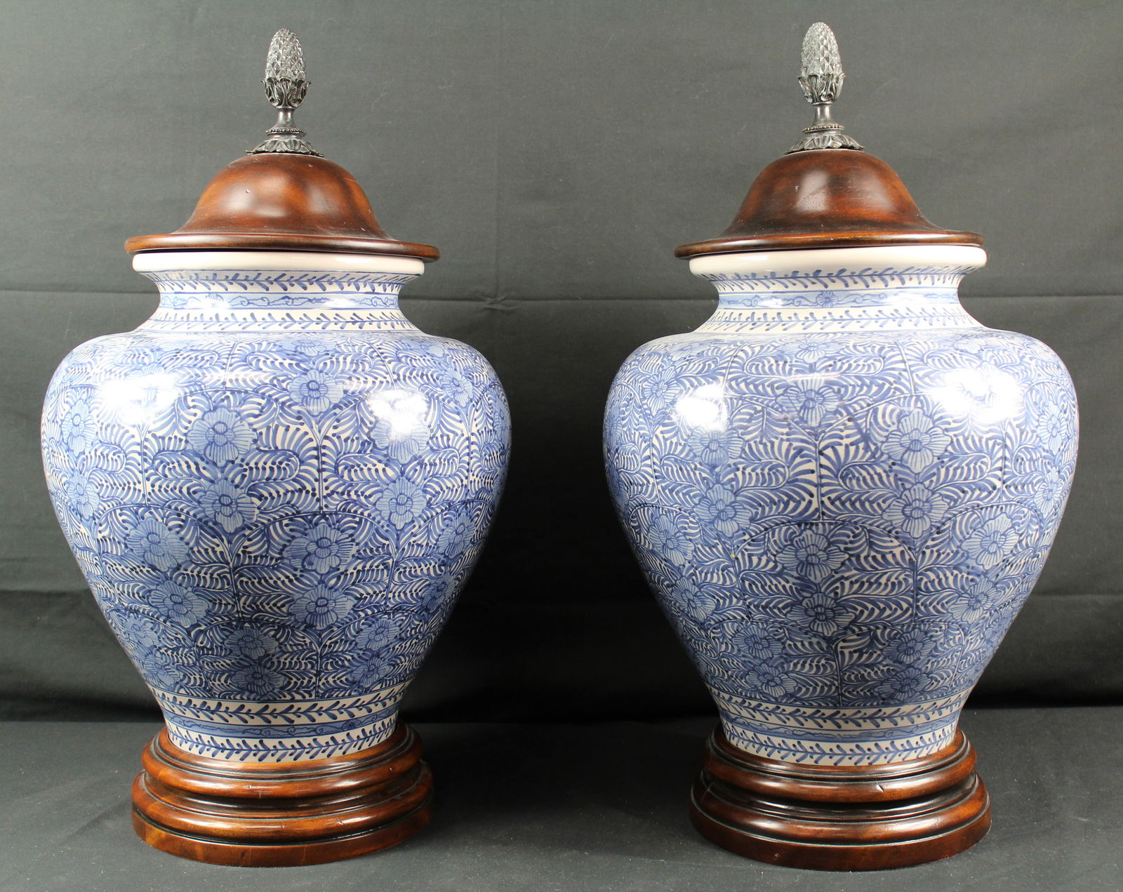 Pair of Theodore Alexander Althorp Blue and White Urns: Pair of Theodore Alexander Althorp Blue and White Urns. Pair of beautiful urns in blue and white colors. Each urn has a floral pattern that has a wood base with wood top and a bronze topper. There is