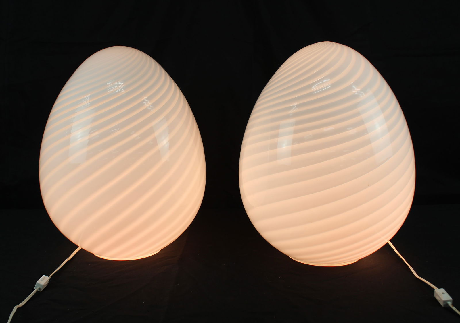 Pair of Murano Swirl Glass Egg Lamps: Pair of Murano Swirl Glass Egg Lamps. Fantastic pair of white glass egg-shaped lamps with a repeating swirl design on them. One lamp has a rubber ring on the bottom of it most likely acting as a