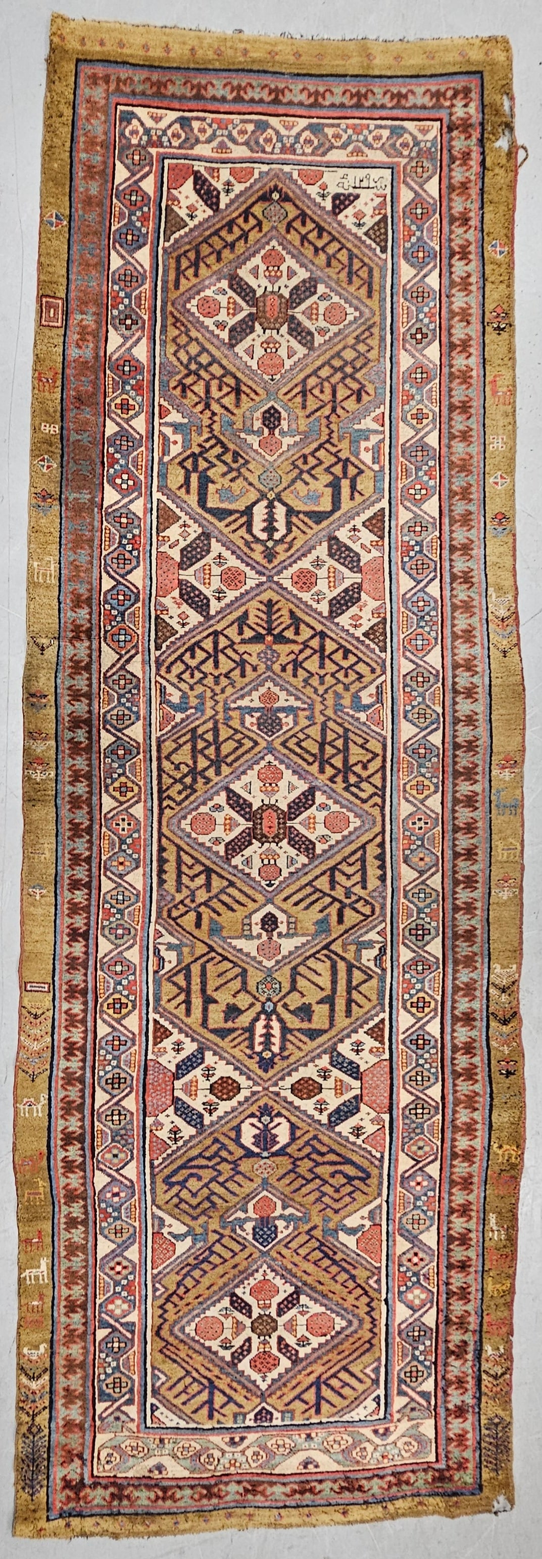 Signed Hand Knotted 4' x 12.5' Runner: Beautiful hand knotted runner with geometric and animal motifs. The rug has beautiful red, blue, and greenish yellow colors. The rug has some holes and light tearing but overall is in good condition.