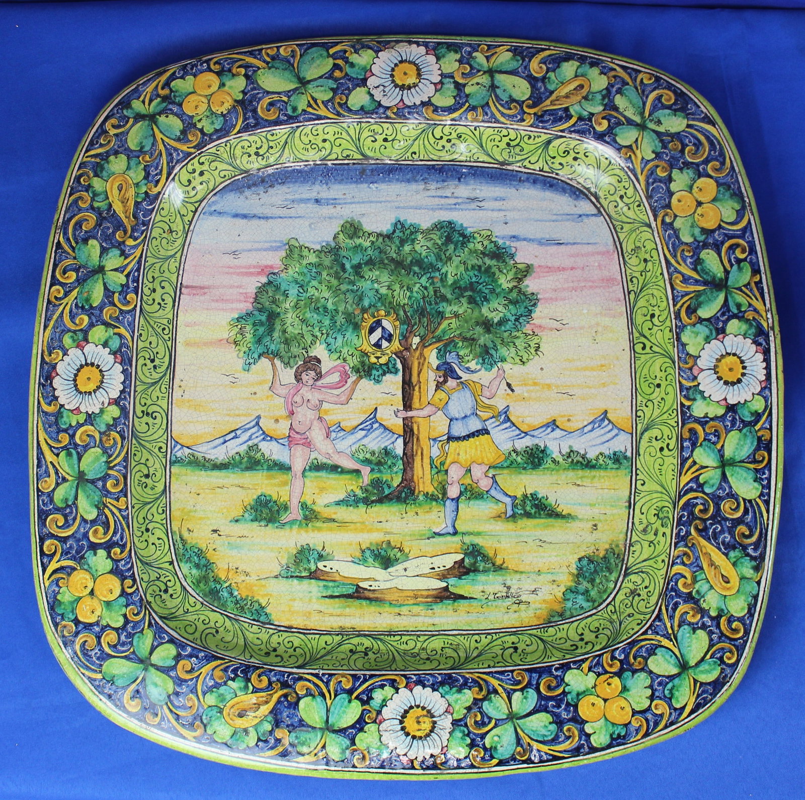 Italian Majolica Charger: Large floral Italian charger depicting a woman and soldier running around a tree and floral designs around the rim in bright green, blue, and yellow colors. The charger is signed in the bottom right c