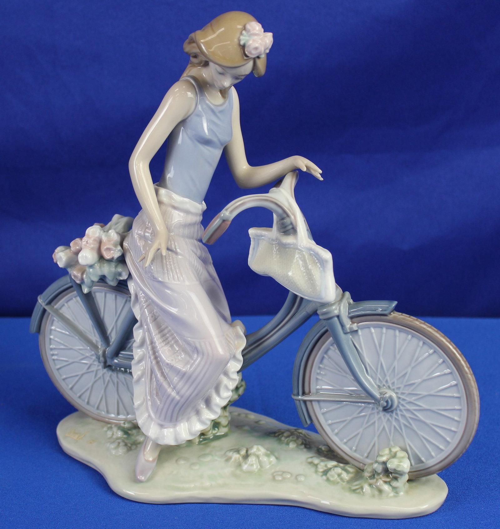 Lladro "Biking in the Country" Figurine: Lladro #5272 "Biking in the Country" figurine featuring a woman in blue and purple clothing on a bicycle. The bottom is labeled Lladro and also says E-30 MY. Overall is in excellent condition. The mea