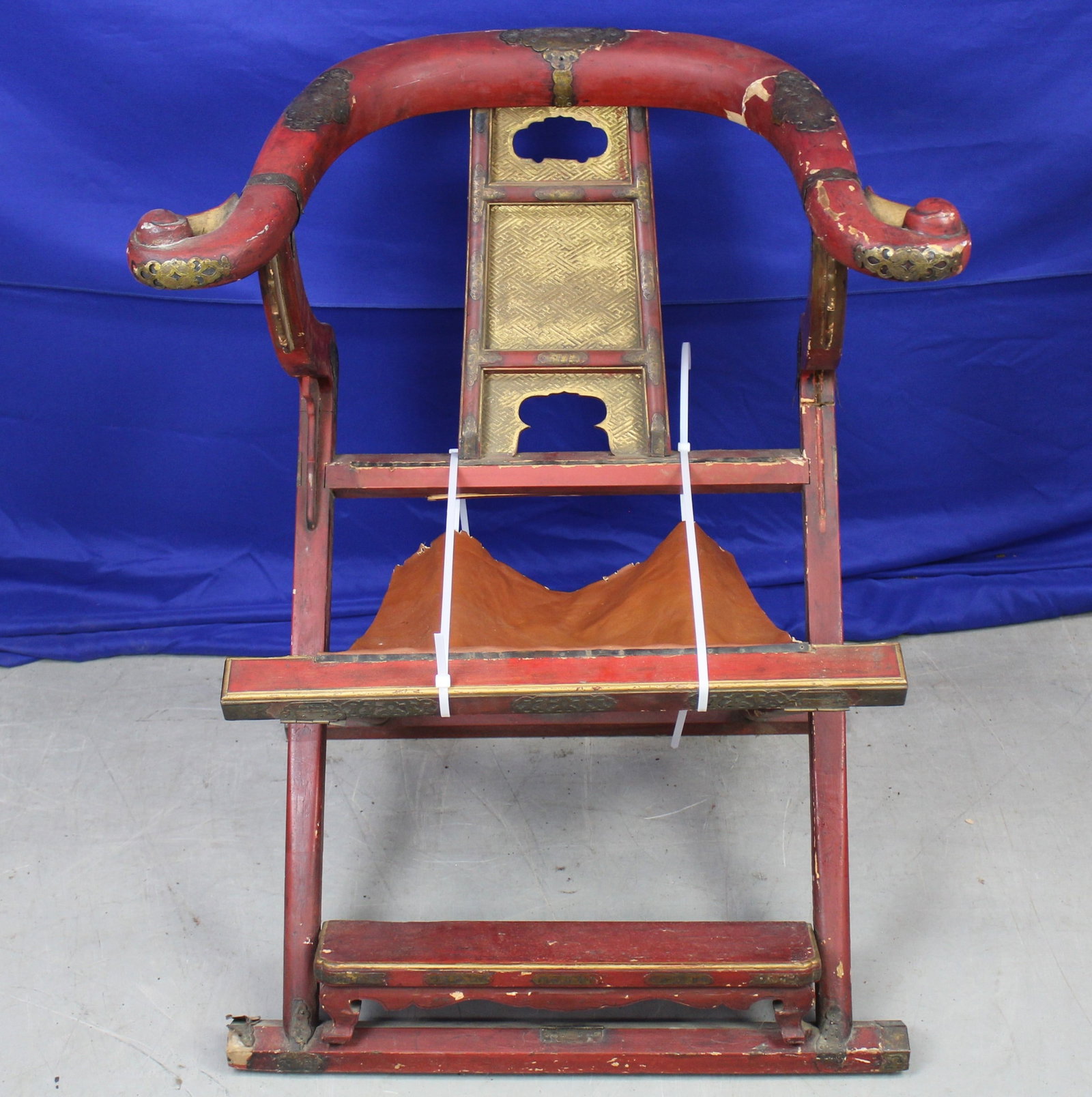 Chinese Red Lacquer Horseshoe Folding Chair: Chinese hand painted red folding wood chair with gold tone accents. To keIt currently has zipties to keep it folded out. The fabric used as the seat is present but is not attached to one side and one 
