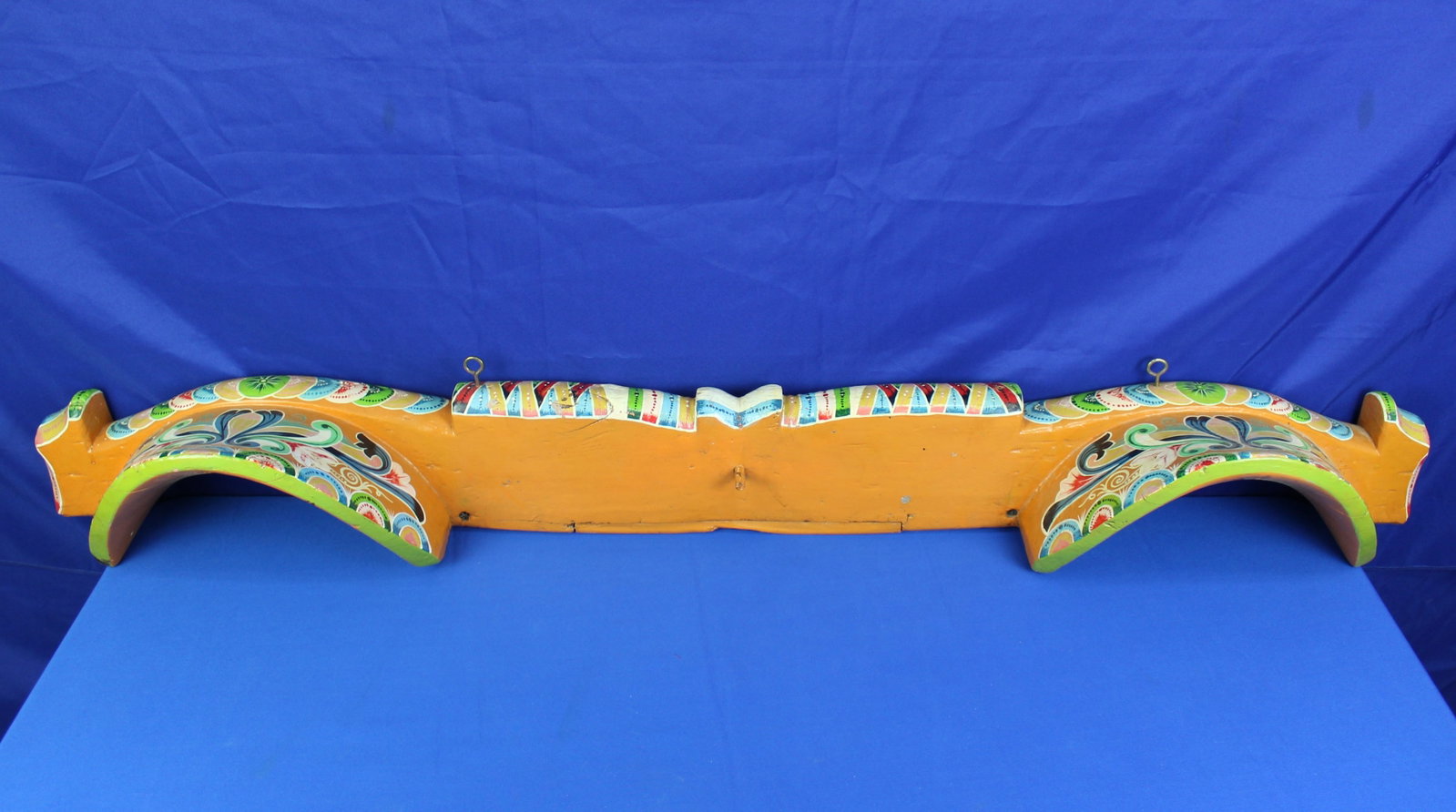 Costa Rican Ox Cart Yoke: Bright colorful orange Costa Rican hand painted wood ox cart yoke. The yoke has painted floral designs with bright green, blue, and red colors. The yoke has some natural cracking in the wood, but