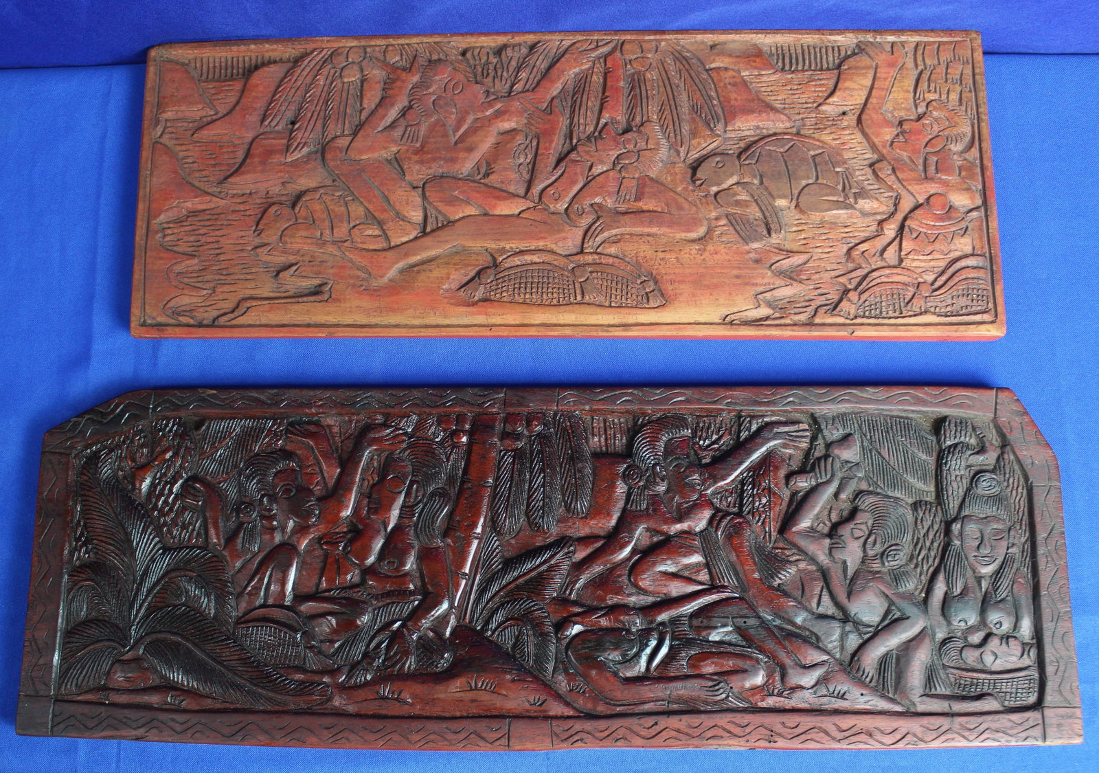 Two Small Wood Carved Panels: Two African carved wood panels the first depicting women surrounded by trees and fauna and the second depicting women relaxing on a beach by water with a turtle. The first panel has some light fading 