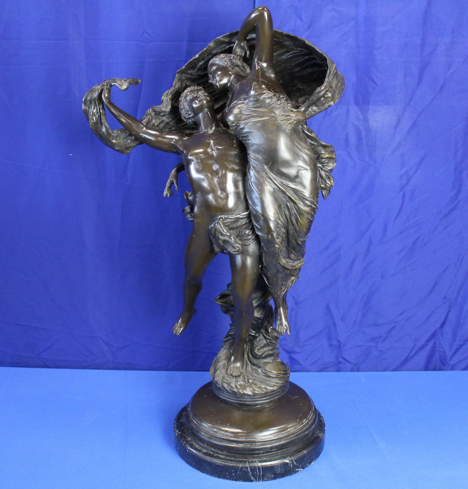 After Eugene Marioton Bronze Dancing Young Lovers Statue: Bronze statue of a lady and a man dancing with flowing ribbon. The bottom of the ribbon on the bronze base of the statue is signed by the artist, Eugene Marioton. The statue is on a black marble base.
