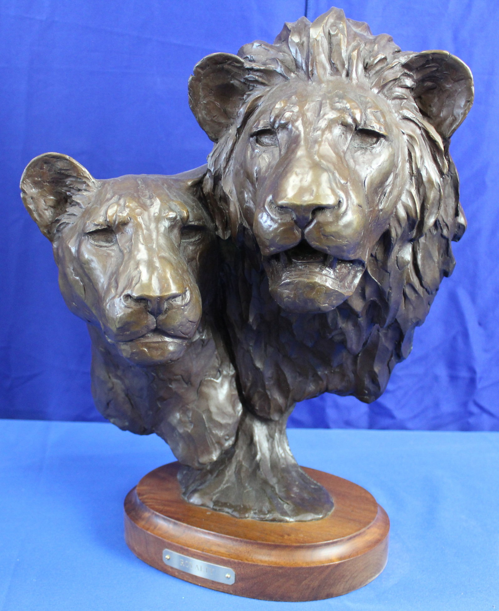 Melvin Johansen Royalty Bronze Lions Bust: Bronze bust of two lions on a wood base with a plaque titled "Royalty". The bust was done by Melvin Johansen and is signed and numbered 9 out of 18 on the back of the lions. Overall the lions are in e