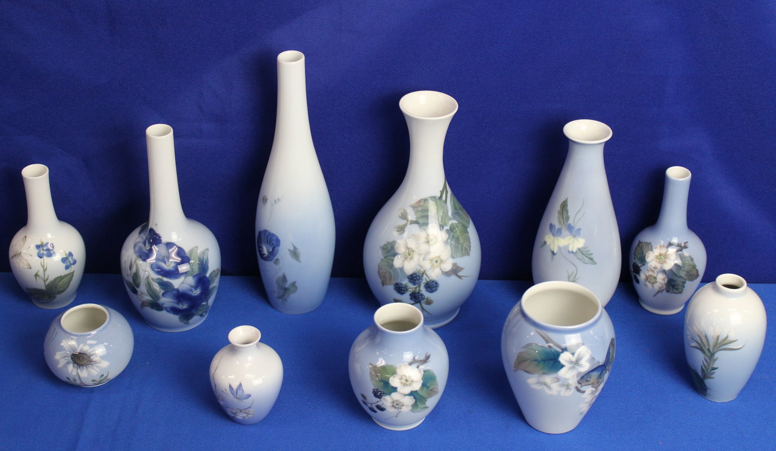 Lot of Royal Copenhagen Vases: Collection of 11 Royal Copenhagen vases of different sizes with designs of flowers and butterflies with blue and white base colors. Every vase has the Royal Copenhagen label on the bottoms. Overall