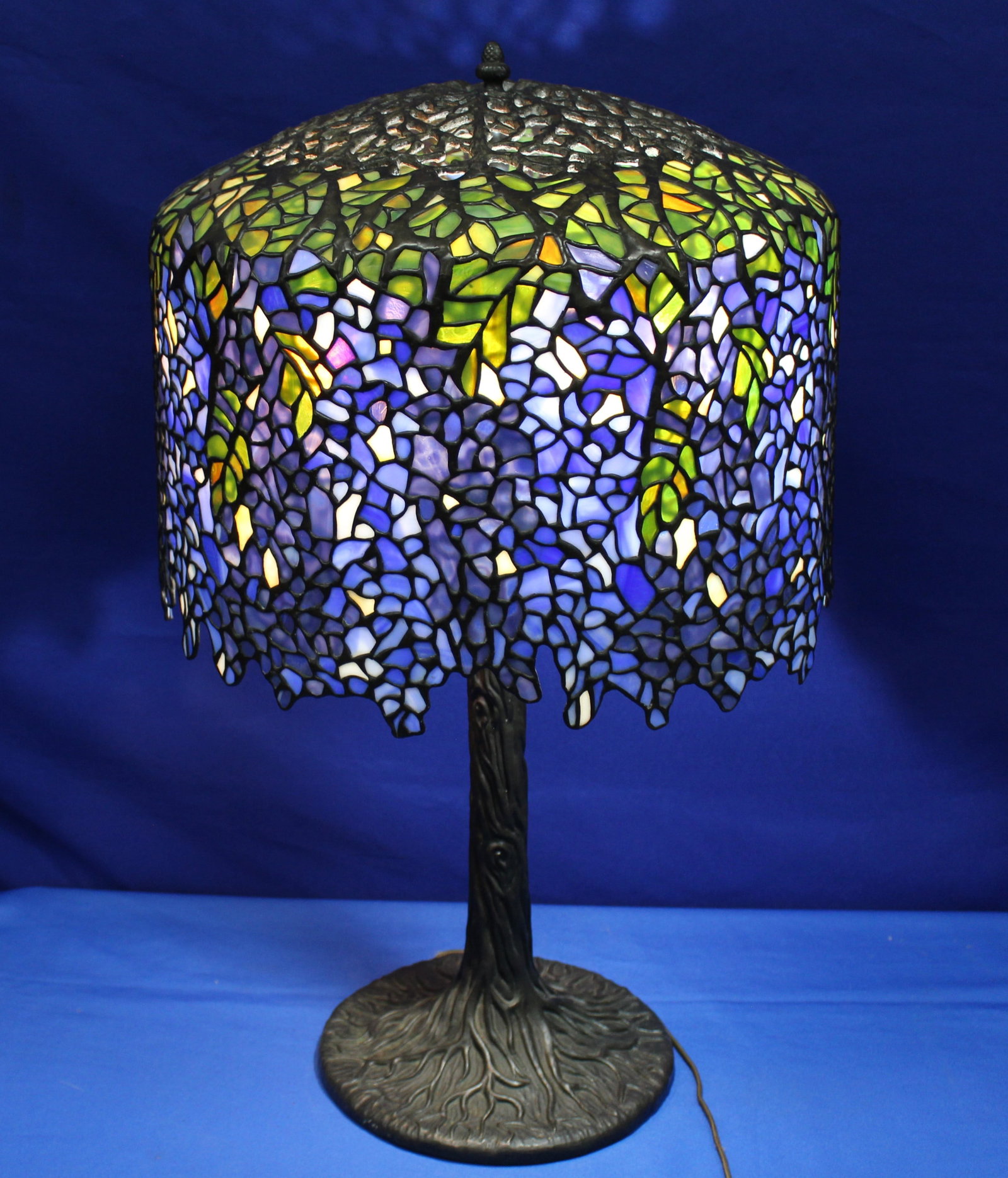 Tiffany Style Bronze Lamp with Blue Wisteria Style Shade: Beautiful Tiffany style lamp with a blue glass shade and a bronze base in the style of a tree. The lamp is fully functioning and is in excellent condition. The measurements are not including the shade
