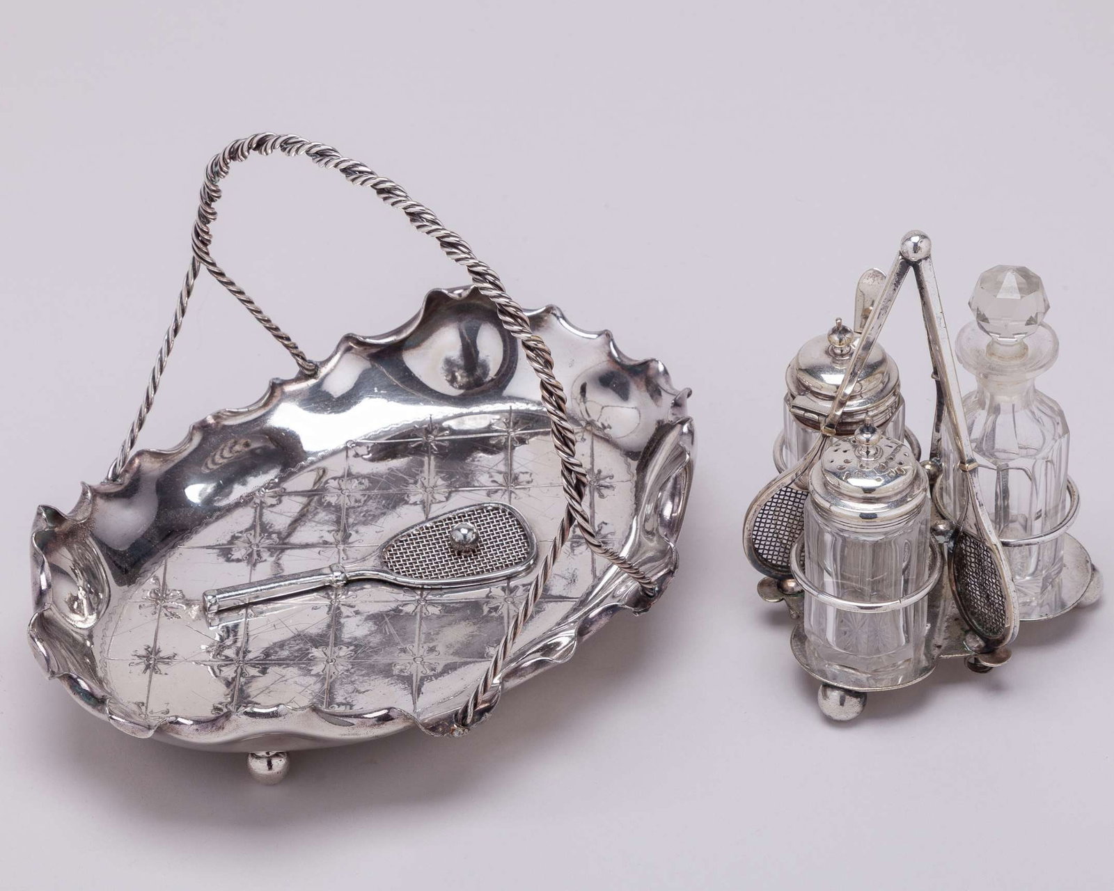 A white-metal tennis cruet set: A white-metal tennis cruet set, with three tennis rackets and ball finial, and a white-metal dish, modelled with tennis racket and ball by Simpson Hall and Miller & Co 