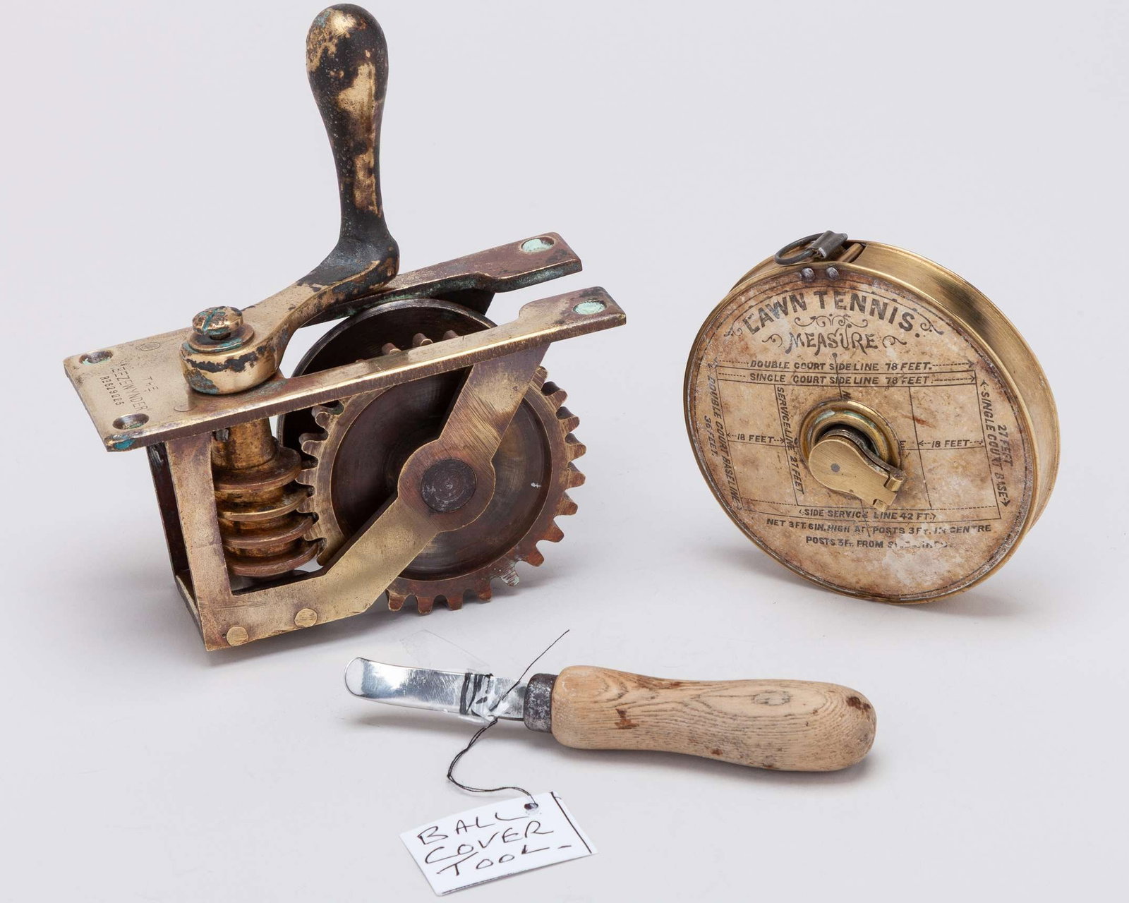 An early brass Lawn Tennis measure, the face with applied label detailing the court shape: An early brass Lawn Tennis measure, the face with applied label detailing the court shape and dimensions, label scuffed and stained, an early tennis ball smoothing tool and, "The Eezewynder" stamped