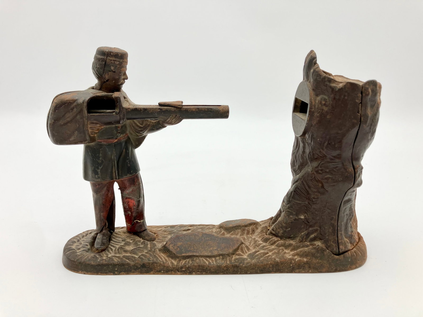 Antique Creedmore Cast Iron Mechanical bank - Man with Rifle: This bank functions by placing a coin on the rifle and cocking it backwards, then launching the coin into the hollowed tree by pressing the man's foot.
