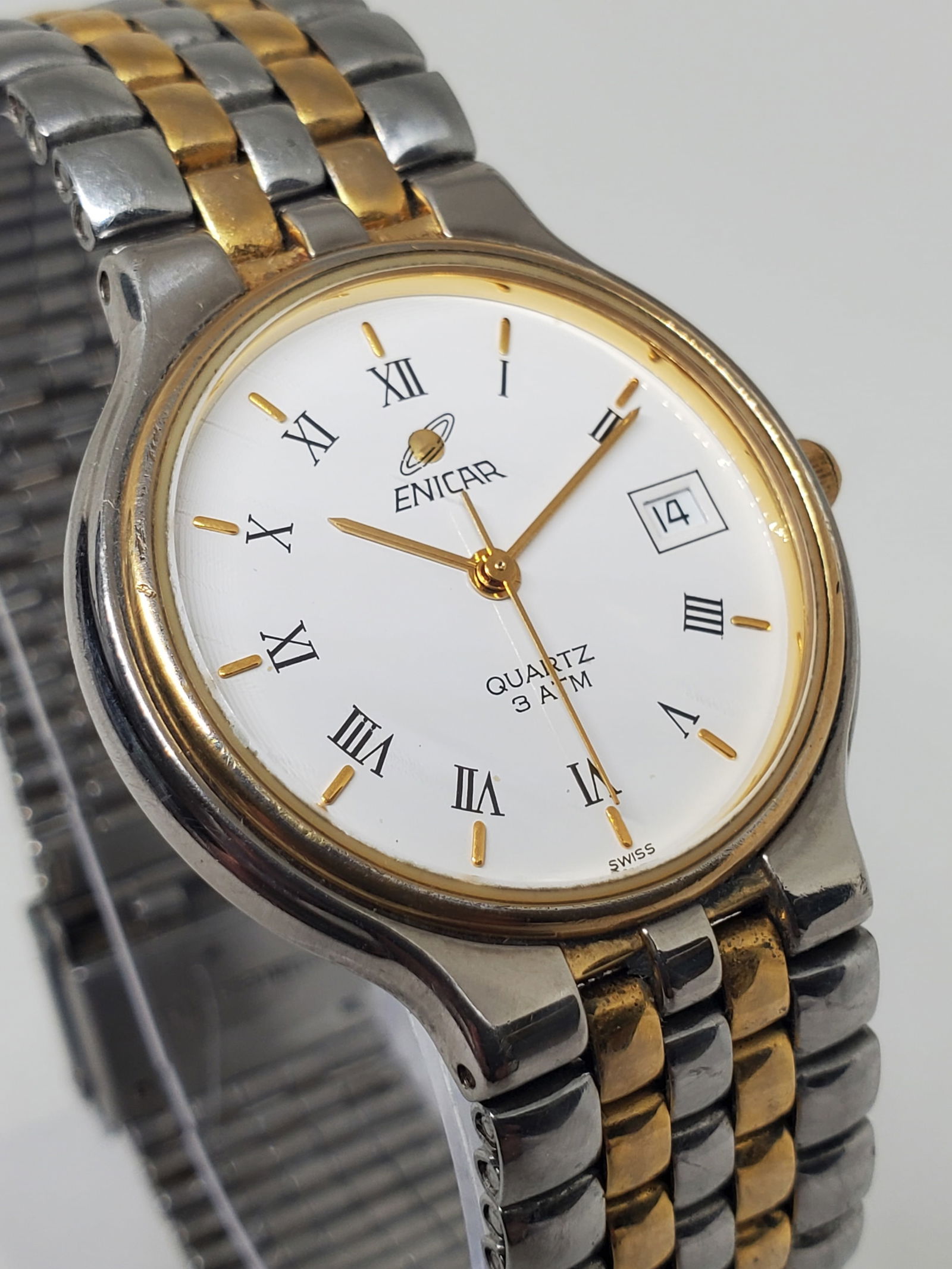 Enicar 955.359 Swiss Quartz Dress Watch Two Tone Date 32mm, late 1980s to early 1990s: This elegant Enicar model 955.359 showcases classic Swiss prestige with a refined dress aesthetic, featuring a silver tone case with a dual tone bezel, a clean white dial with gold markers, and a prac
