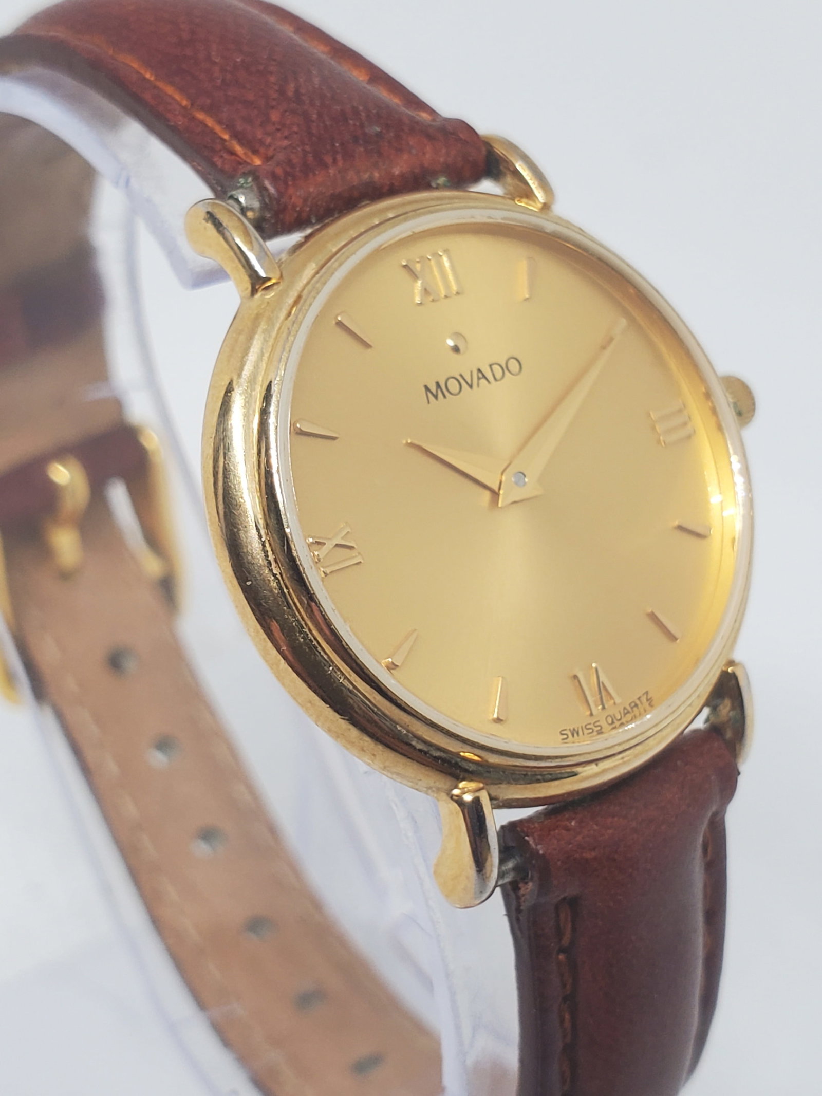 Vintage Movado Swiss Quartz Gold Dial Dress Watch 28mm Leather, 1990s: This elegant Movado dress watch showcases timeless prestige and refined Swiss design, featuring a gold plated case, gold dial, and gold markers paired with a classic leather bracelet sized at 7?, offe