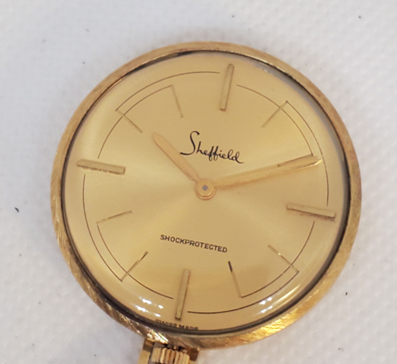 Vintage Sheffield Swiss Pendant Watch Gold Dial 34mm Manual Wind, circa late 1960s to early 1970s: This elegant Sheffield Swiss made pendant watch exudes timeless sophistication and vintage charm. Featuring a gold plated 34mm case and a sunburst gold tone dial with minimalist stick indices, it perf