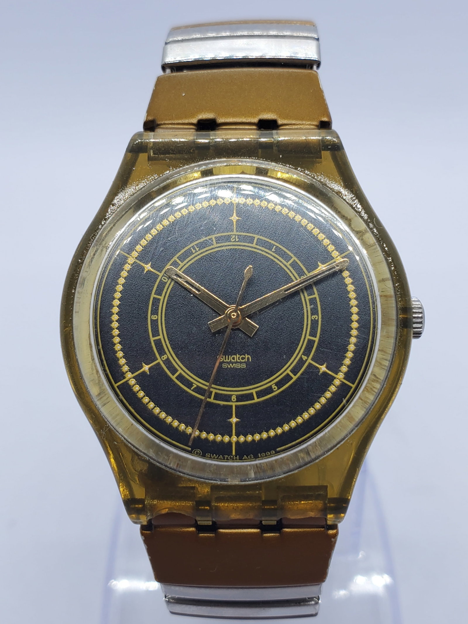 Swatch Originals Gent Gold Translucent Quartz 34mm, 1999, Working: Swatch Originals Gent GK100 is a distinctive Swiss quartz timepiece featuring a translucent amber tone case paired with a refined navy blue dial accented by elegant gold concentric rings and minimalis