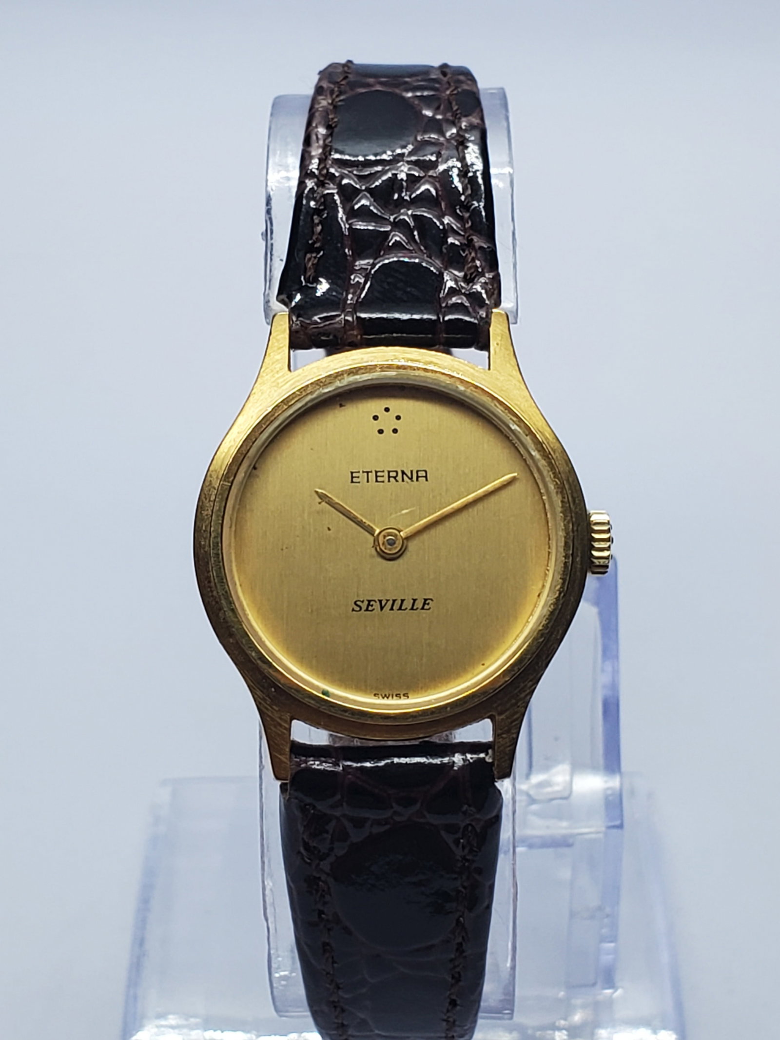 Vintage Eterna Seville Gold Plated Manual Watch, 23mm, 1970s, Running: This elegant vintage Eterna Seville Model 335.6030.25 is a refined Swiss ladies dress watch with a 23 mm gold-plated case, warm gold dial, and 6.75-inch brown leather bracelet. The hand-wound mechanic