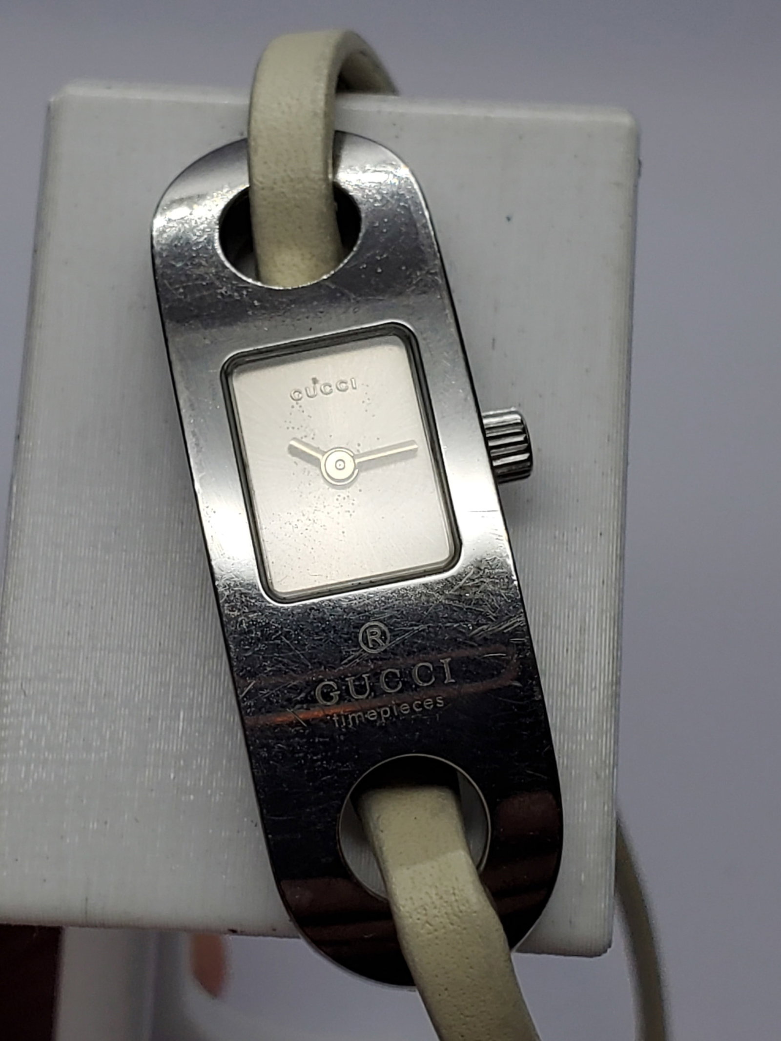 Vintage Gucci 6100L Wrap Leather Bracelet Watch w/Papers, 14x41mm, 2007, Running: Authentic Gucci 6100L Swiss made quartz dress watch featuring a polished silver tone stainless steel case with a refined sunburst silver dial, minimalist baton hands, and Gucci signature styling. This