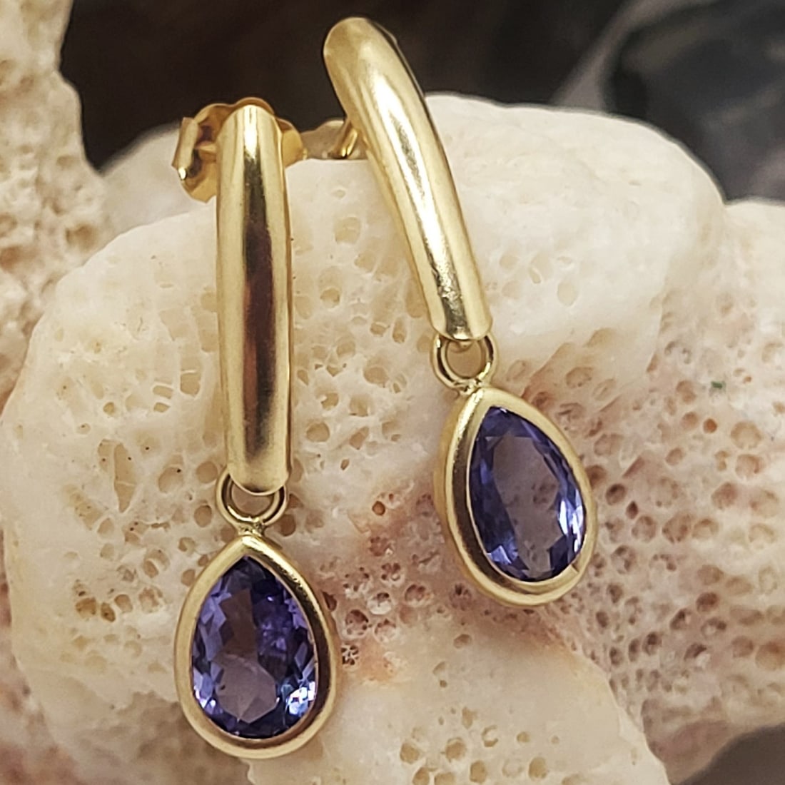 14K Yellow Gold Dangling Tanzanite Earrings: Setting: 14K Yellow Gold Main Gemstone: Genuine Tanzanite Closure: Posts and Friction Backs This pair of casually elegant earrings has 1.30 carats total weight of pear-cut, genuine