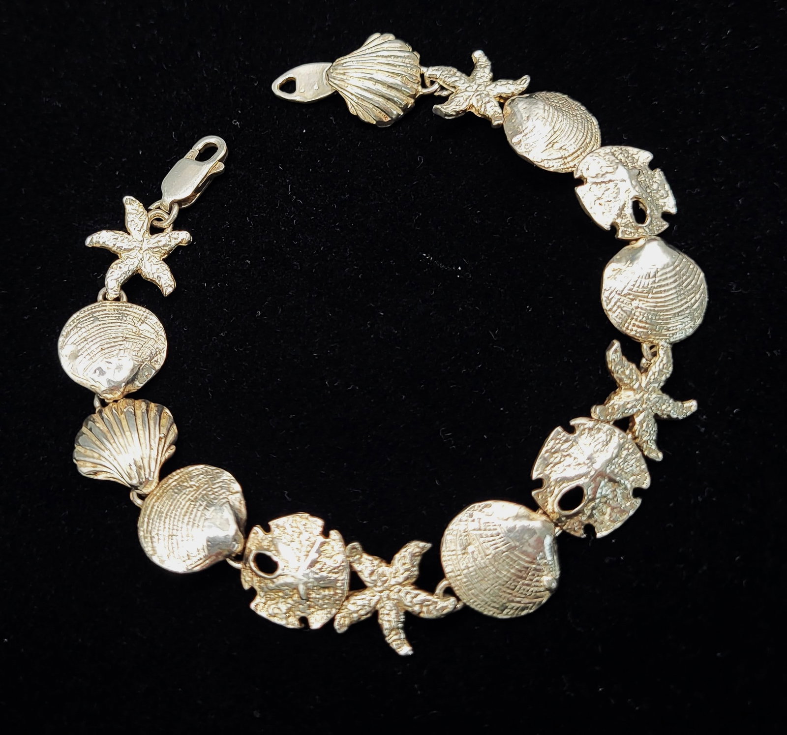 Seashells, Sand Dollars, Starfish, and Scallops Bracelet: Cast in: Sterling Silver .925 Length: 7.5" Closure: Lobster Clasp Weight: 14.4g This is a sterling silver bracelet with a nautical motif. Each link of the bracelet represents a cockle shell, sand doll