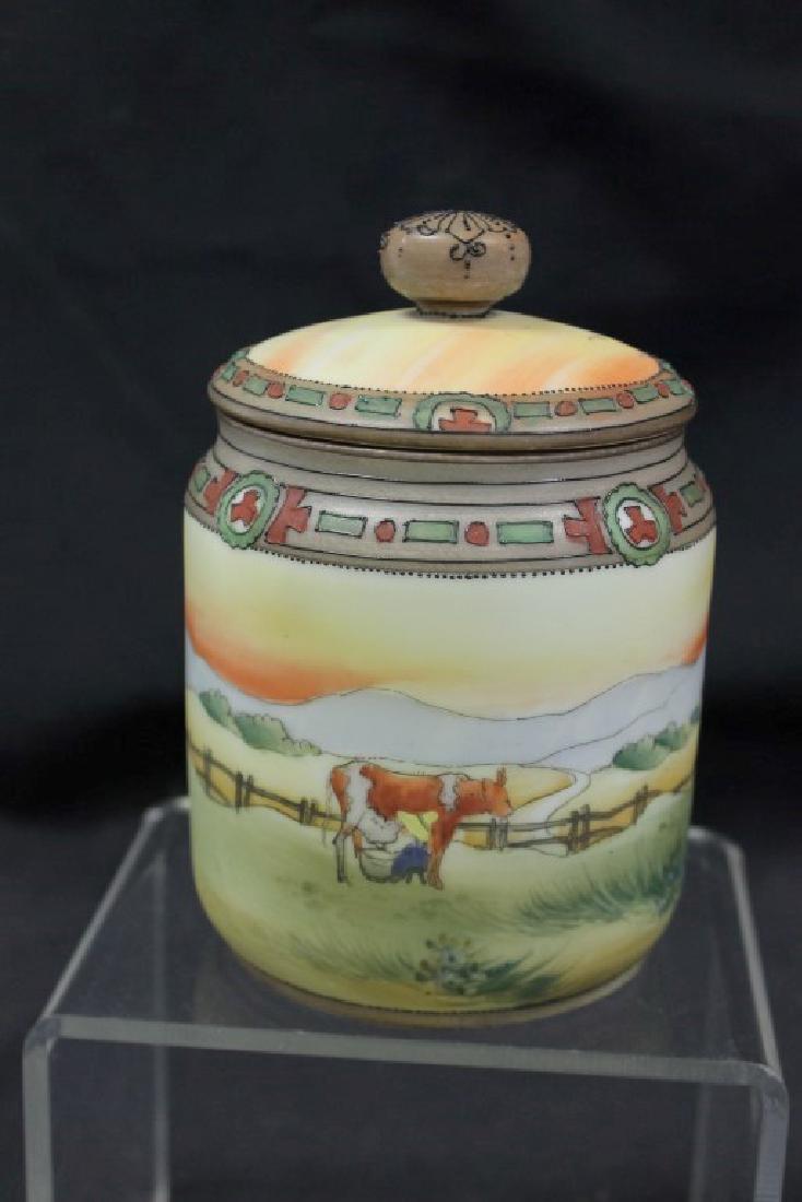 Nippon Green M in wreath 5 3/4" humidor with maiden: Nippon Green M in wreath 5 3/4" humidor with maiden milking a cow in a landscape. Minor bead loss; minor interior rim nicks; line on sponge holder; nick on inner rim of lid.