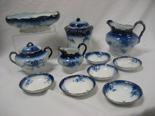 La Belle flow blue china: (6) 4 3/4" berry bowls;: La Belle flow blue china: (6) 4 3/4" berry bowls; creamer; covered sugar; 7" milk pitcher; 10" rolled rim oval bowl; 7 1/2" cracker jar with unglazed base, marked K, minor interior stain. A small line