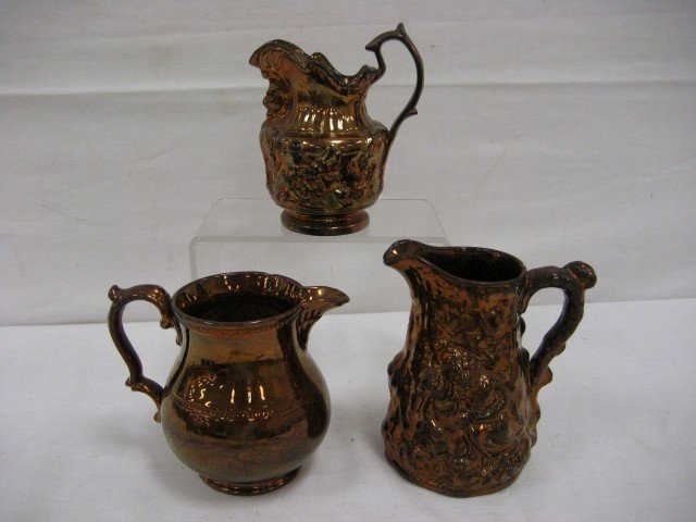 Copper lustre: 5 1/4" pitcher with beading, rim c: Copper lustre: 5 1/4" pitcher with beading, rim chip; 6"pitcher with modled monkey and mask below spout; 6 3/8" pitcher with molded mother and child with grapes, leaf and vine.