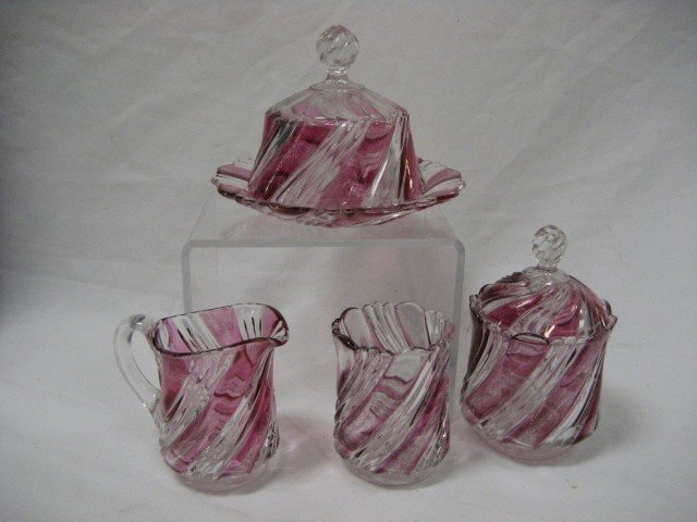 Four (4) piece swirl ruby flashed table set. Spoo: Four (4) piece swirl ruby flashed table set. Spooner with chips on vase, butter with minor rim nicks
