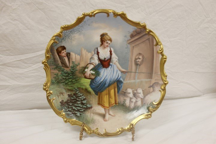 Limoges 15 1/2" charger signed Muville showing a young: Limoges 15 1/2" charger signed Muville showing a young lady with sheep at a fountain carrying a basket of eggs as a young man looks on. Heavy gold border decoration, partial back stamp.