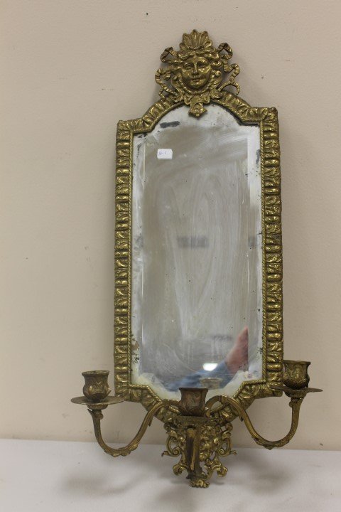 Brass wall sconce with beveled mirror and three candle: Brass wall sconce with beveled mirror and three candle arms. Rope border on molded border of mirror, with ladies heas at top and laughing man at base. Marked "H-P" on reverse. 23 1/2" tall, 8 5/8" wid