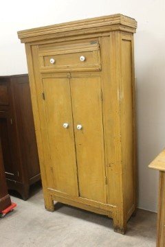 Early primitive tall cupboard in mustard paint. One: Early primitive tall cupboard in mustard paint. One drawer over two doors, with molded cornice. 70" tall, 37" wide, 14" deep.
