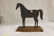 Mounted sheet iron horse on wooden base, with strap at