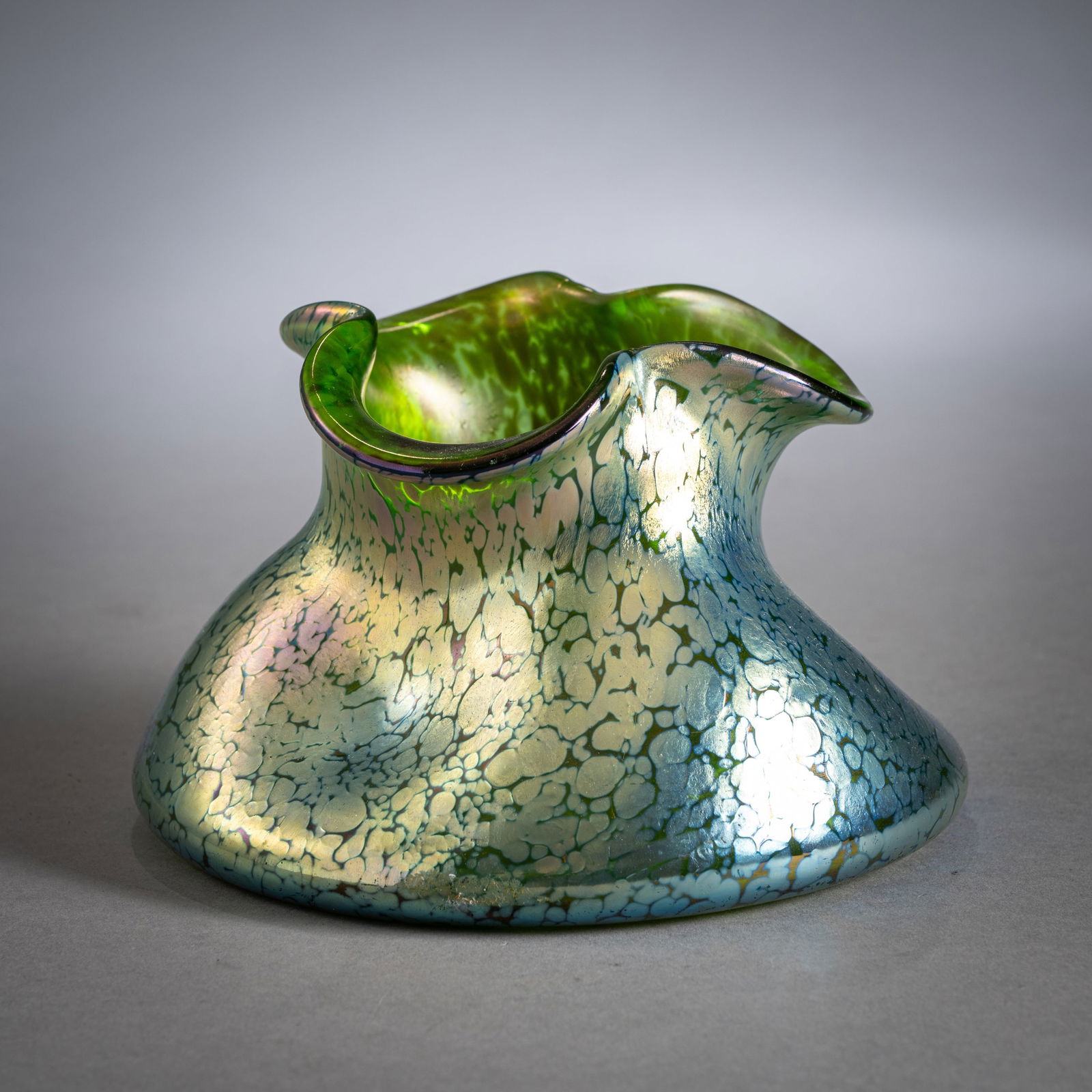 A LOETZ PAPILLON PATTERN VASE: A LOETZ PAPILLON PATTERN VASELoetz Wwe., Klostermühle, circa 1900H. 11,5 cmGreen glass with melted silver crumbling, iridescent rim. A minimal chip (approx. 1 mm) on the rim.Vase mit Papillon Dek