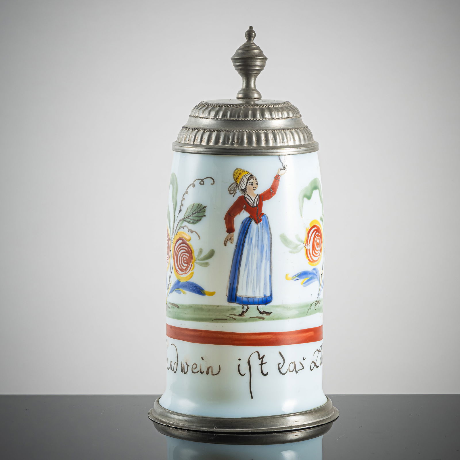 A PEWTER MOUTNED MILK GLASS TANKARD: A PEWTER MOUTNED MILK GLASS TANKARDearly 19th centuryH. 21 cmEnamel painted milk glass with woman drinking wine and inscription. Minute hairline crack to handle.Humpen aus Milchglas mit WeintrinkerinA
