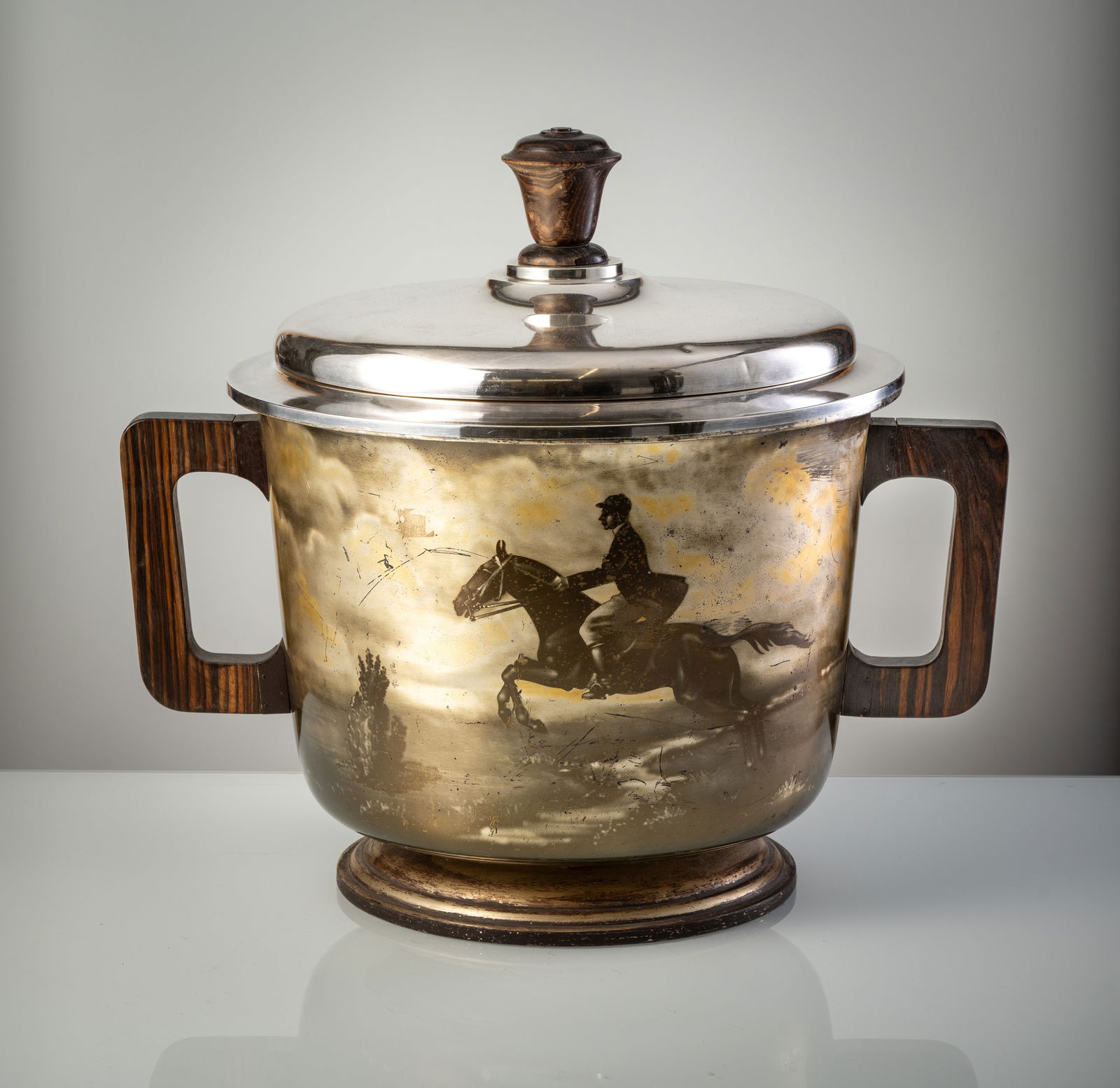 A LARGE BOTTLE COOLER WITH HORSEMAN: A LARGE BOTTLE COOLER WITH HORSEMAN England, 20th century. D. 46 cm/ H. 50 cm Metal, printed and silver-plated. Wooden handleS. Dented, rubbed, oxidised.Großer Flaschenkühler mit