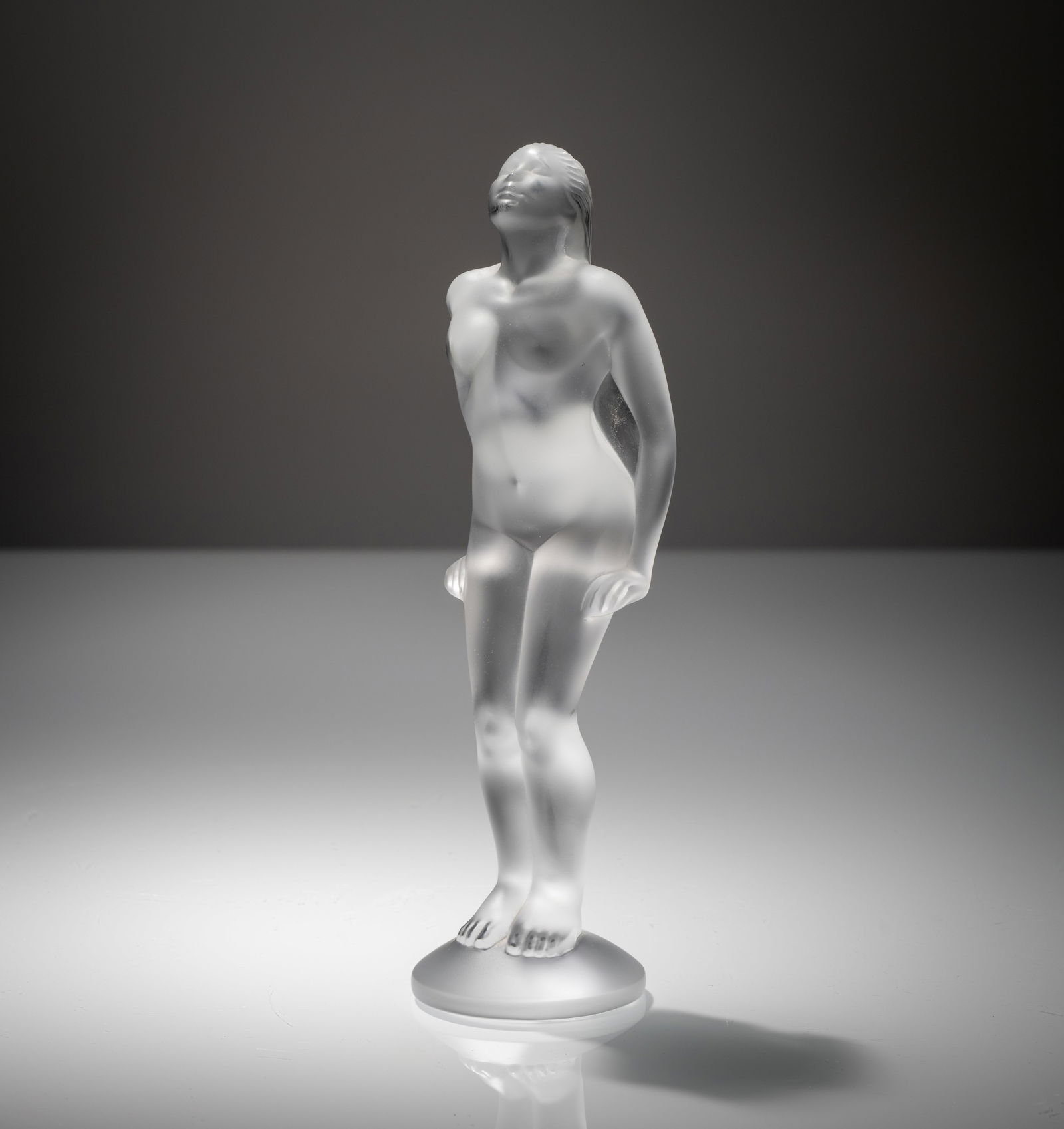 A GLASS FIGURE OF A FEMALE NUDE: A GLASS FIGURE OF A FEMALE NUDE Lalique France H. 19,5 cm Colourless, matted glass with etched signature to bottom.Figur - Weiblicher Akt Lalique, France H. 19,5 cm Farbloses, mattiertes Glas, am