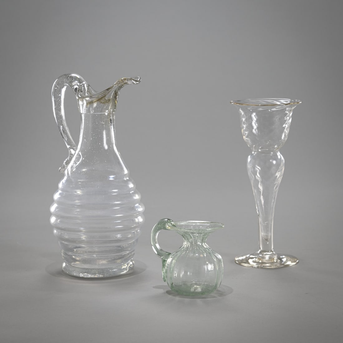 TWO SMALL JARS AND A GLASS VASE: TWO SMALL JARS AND A GLASS VASE 18TH/19TH CT H. 6-20 cm Colourless and green glass.Zwei Krüge und Glasvase 18./19. Jh. H. 6-20 cm Farbloses und grünes Glas, passig gedreht.