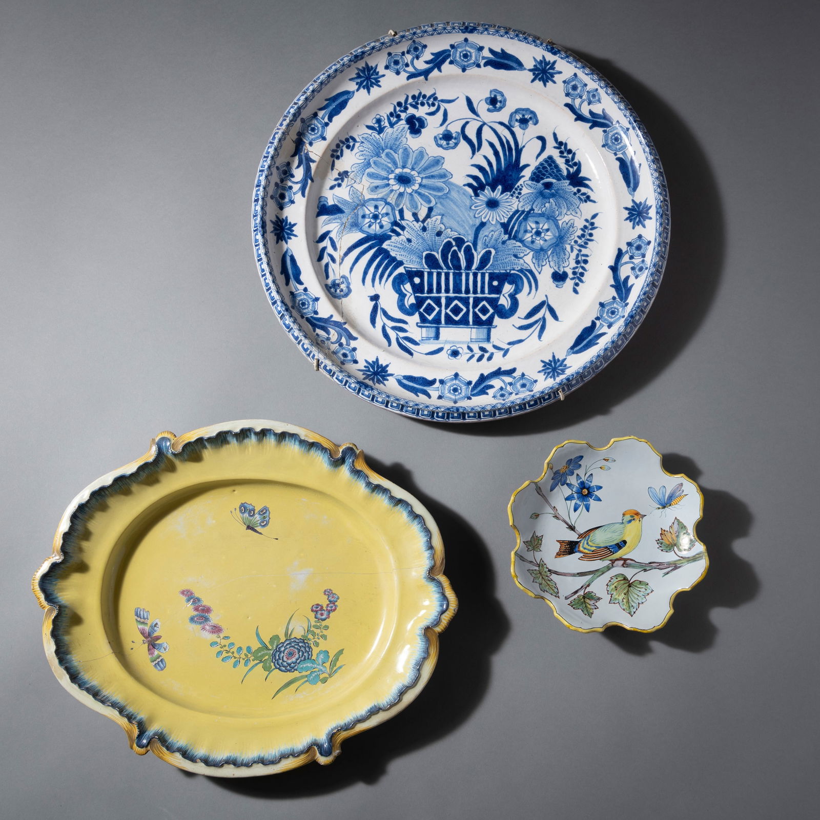 TWO FAIENCE DISHES AND A PLATE: TWO FAIENCE DISHES AND A PLATE Hoechst and Delft, 18th century D. 21/45 cm Oval dish with green wheel mark with L. Comes with a plate with bird, 20th century. Restorations and chipsOvalplatte,