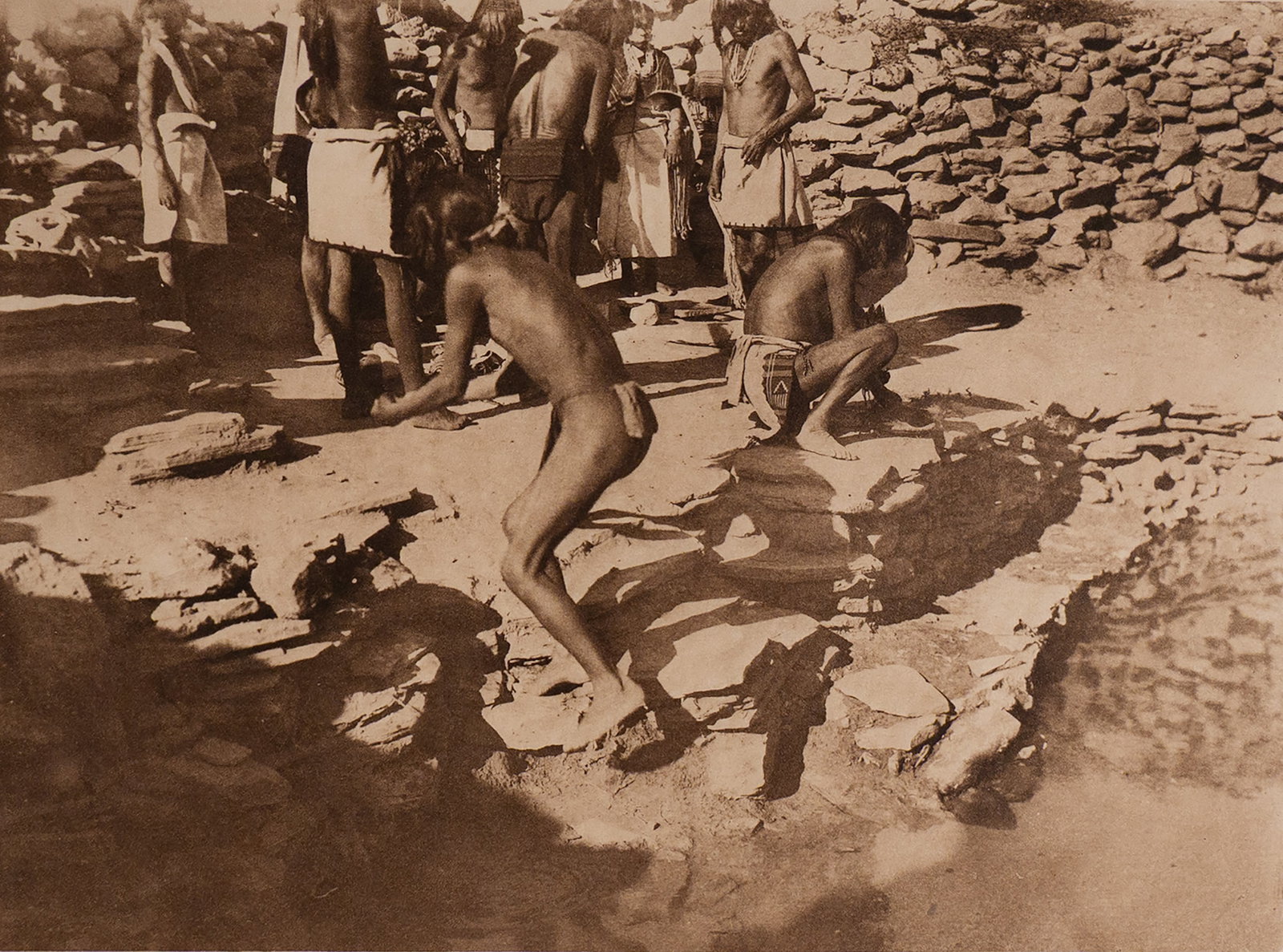 Flute Dancers Dressing at Kachina House: This image offers an exceptional view into the sacred and ceremonial life of the Hopi. Two young men in the foreground are shown in preparation for the Flute Ceremony—a rain-invoking ritual of great