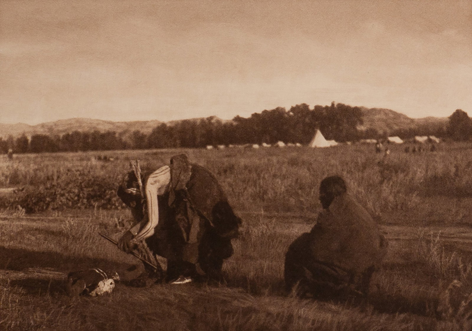Offering Pipe to the Skull - Cheyenne: In this solemn and symbolically rich image, a Cheyenne man kneels in an open field, extending a pipe toward a buffalo skull resting on the earth. Another figure sits silently beside him, and in the di