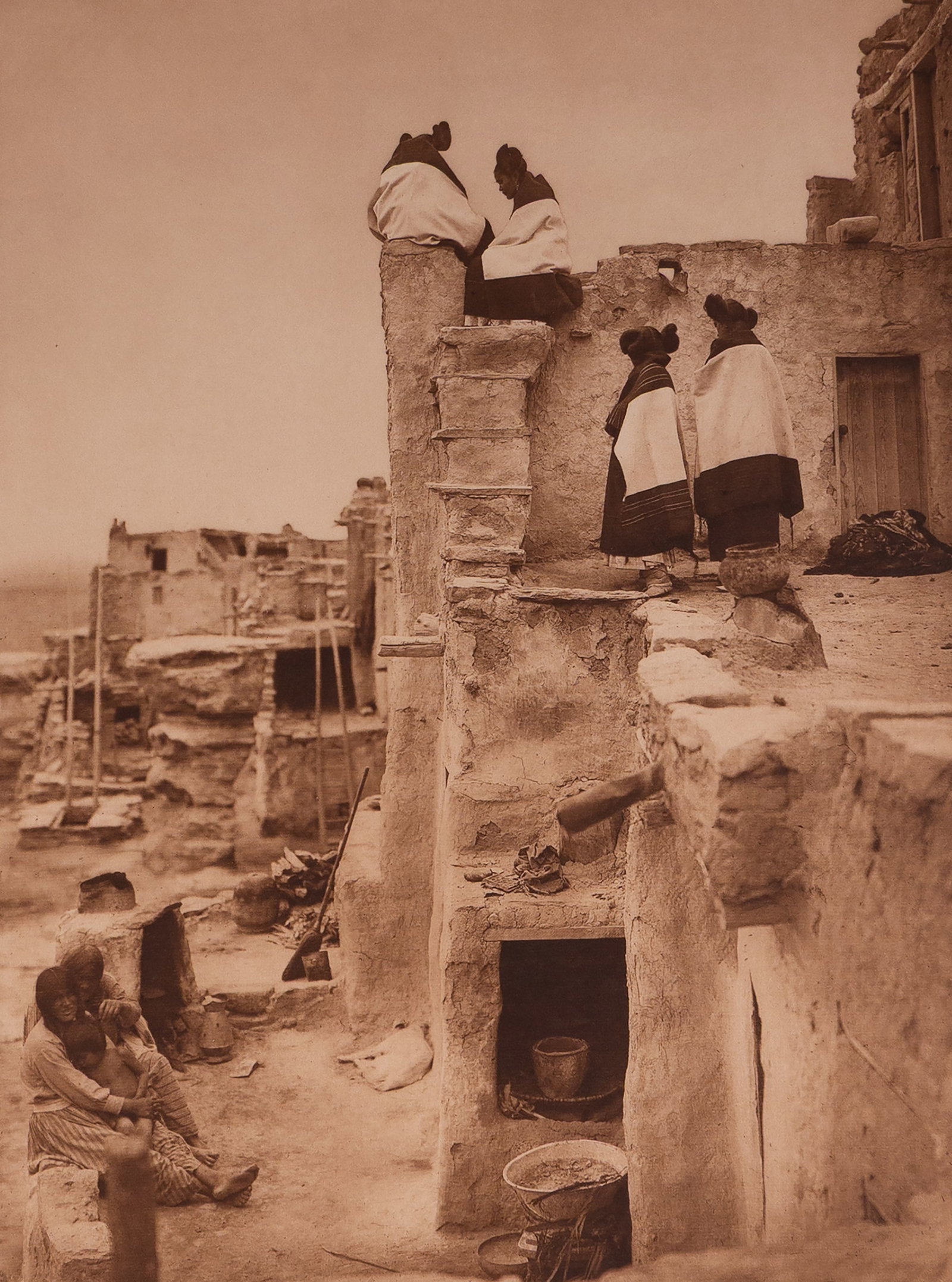 On the Housetop: This is printed on Japanese Gampi tissue paper. Curtis' On the Housetop captures a rare and layered domestic moment in the Hopi village of Walpi atop First Mesa. Several young women, identifiable by t