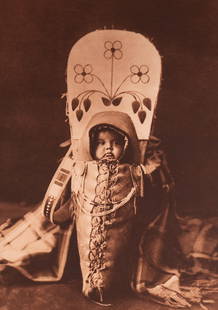 Nez Perce Babe: A tender and intimate portrait of an infant swaddled in a traditional Nez Perce cradleboard, the child’s gaze turned gently toward the light. Curtis’s composition highlights the protective craftsm