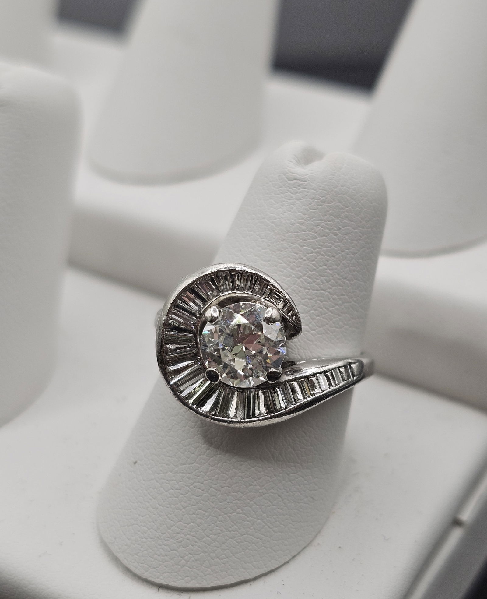 Platinum and Diamond Swirl Ring: Stones: European-cut diamond weighing approximately 1.00 carat; baguette-cut diamonds weighing a total of approximately 0.65 caratMetal: PlatinumGross Weight: 7.90 gramsSize: 6-1/4