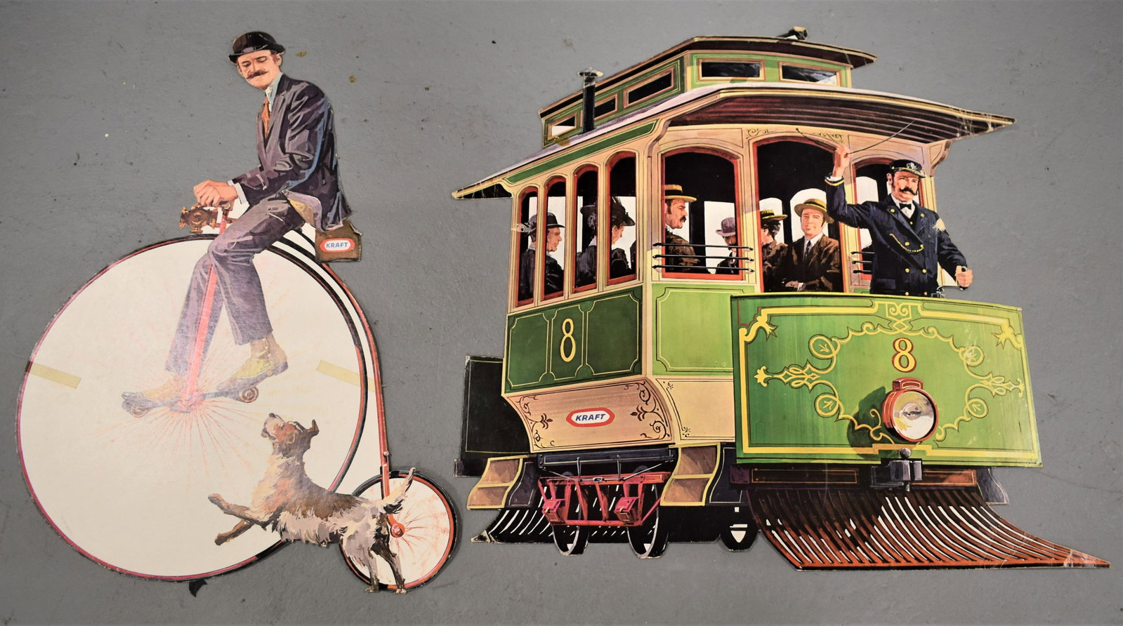 (2) Kraft Cut Out Card Advertisement Displays: (2) VINTAGE KRAFT CHEESE CUT OUT STONE DISPLAYS- MAN ON HIGHWHEEL BIKE (28" X 20 1/2") AND CONDUCTOR ON TROLLEY (27 1/2" X 29"- CREASES, BENDS, WEAR AND LOSSES