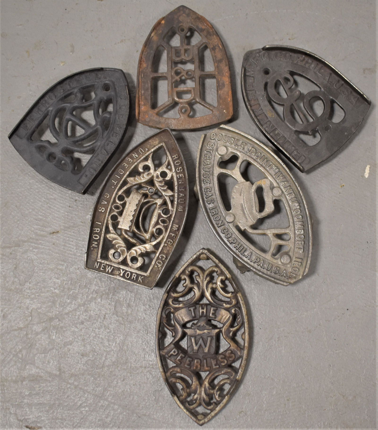 Lot (6) Advertising Cast Iron Trivets: LOT (6) MISC. ADVERTISING CAST IRON TRIVETS - ROSENBAUM, FERROSTEEL, PEERLESS, B AND D, STRAUSE GAS IRON CO., AND ENTERPRISE - VARIOUS SIZES - IMPERFECTIONS