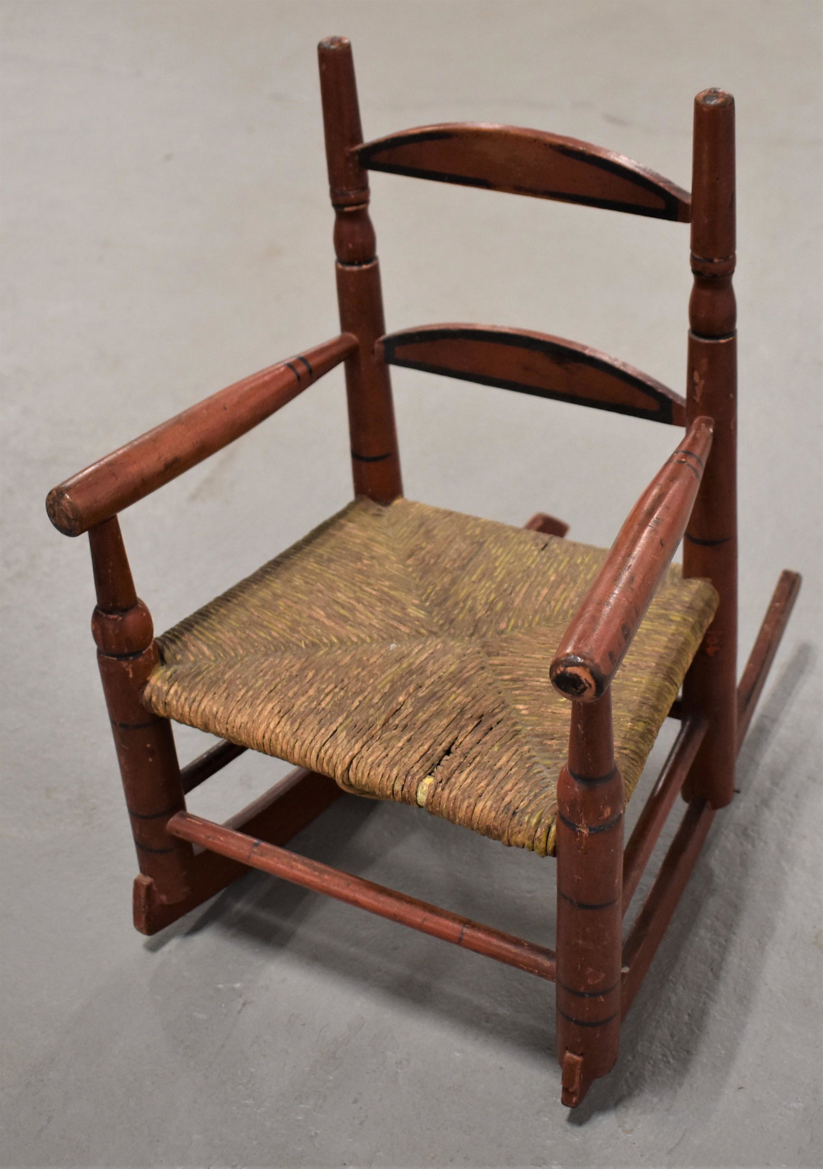 Child's Painted Ladder Back Arm Rocker: LATE 19TH CENTURY EARLY 20TH CENTURY LADDERBACK ARM ROCKER WITH RUSH SEAT IN OLD RED AND BLACK PAINT - 17"T x 11"W x 15" D WITH ROCKERS - WEAR, IMPERFECTIONS
