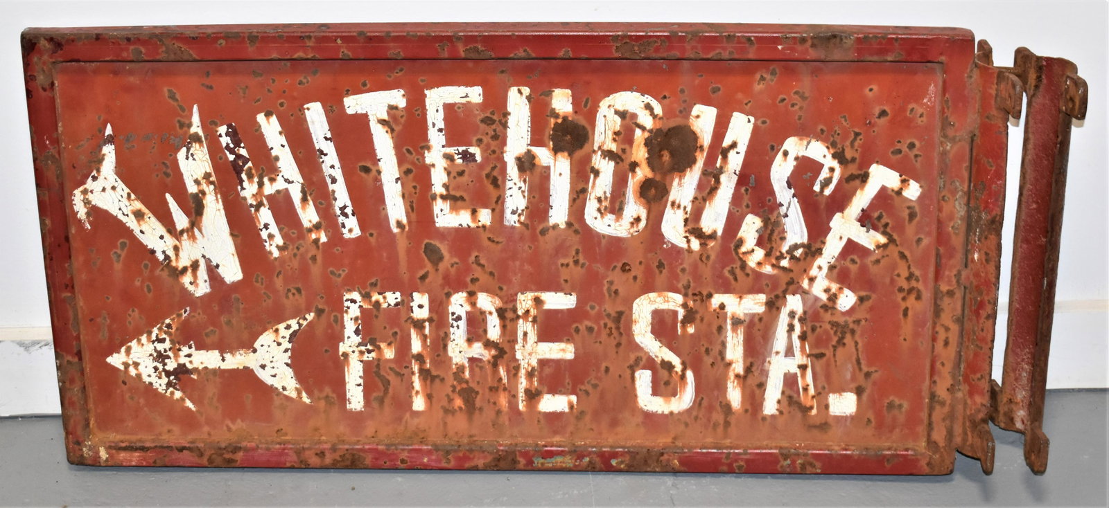 Early 20th Cent Whitehouse Fire Station Sign: EARLY 20TH CENTURY PAINTED SHEET METAL SIGN WITH IRON FRAME FOR MOUNTING - RED WITH WHITE LETTERING "WHITEHOUSE FIRE STA. WITH ARROW - SINGLE SIDED 34"L x 16" - OXIDATION, WEAR AND LOSSES TO PAINT - I