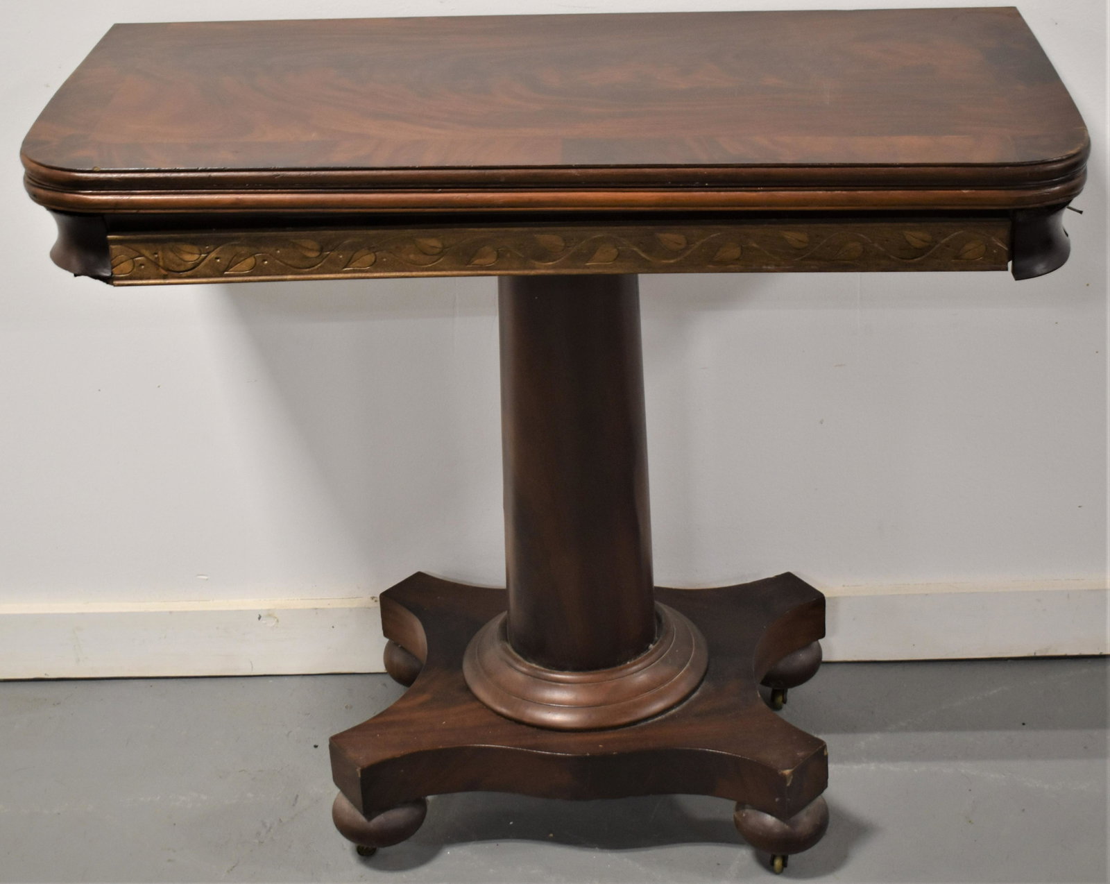 Empire Mahogany Flip Top Card Table: 19TH CENTURY EMPIRE MAHOGANY CENTER PEDESTAL FLIP TOP CARD TABLE WITH CARVED FRONT SKIRT - 30"T x 34 1/4"W x TOP 34 1/2" x 34" - SCRATCHES, WEAR, VENEER LOSSES, SMALL REPAIRS AND IMPERFECTIONS